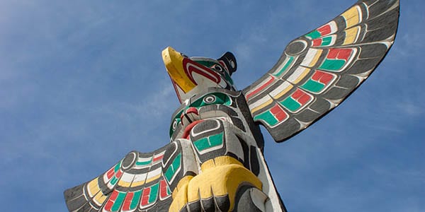 Looking up at a colorful totem pole in the shape of an eagle with green, red and gold coloring.