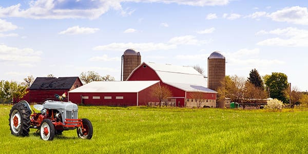 A tractor in the foreground, red barn and brown silos in background.