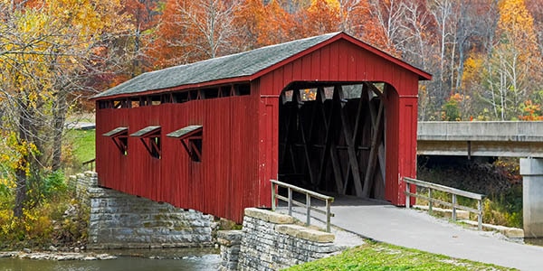 A red covered bridge spans a small river.