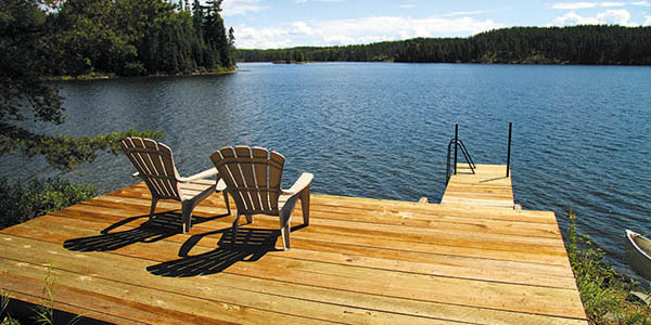 A pair of Adirondack chair on a dock overlooking a lake.