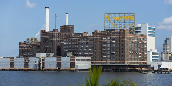 A large factory with the sign, Domino Sugar, sits on a waterfront. 