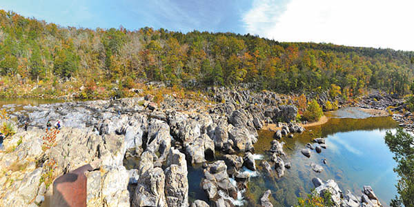 Rugged rock bluff looms over a calm clear pond in the Ozarks