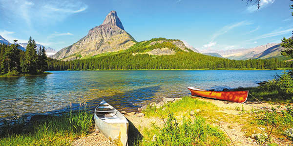 Two canoes rest on the banks of a lake with a mountain in the background.