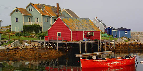 A red boat moored near a dock with a red house on pilings over the water..