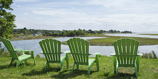 Four empty Adirondack chairs overlook the bend of a curving stream.