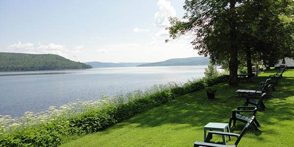 Green deckchairs on a lawn fringed with flowers overlook a wide river.