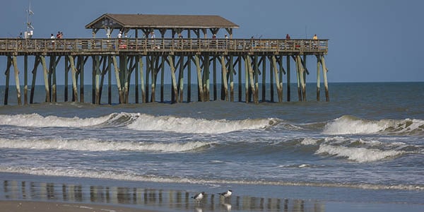 A wooden pier with a-frame canopy at the end juts out into the ocean.