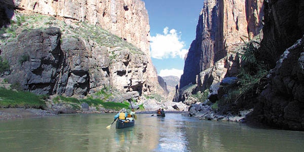 Paddlers in a canoe enter a narrow stretch of river bordered by high, sheer rock walls.