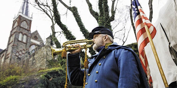 A trumpet player in a Union Uniform near an American flag.