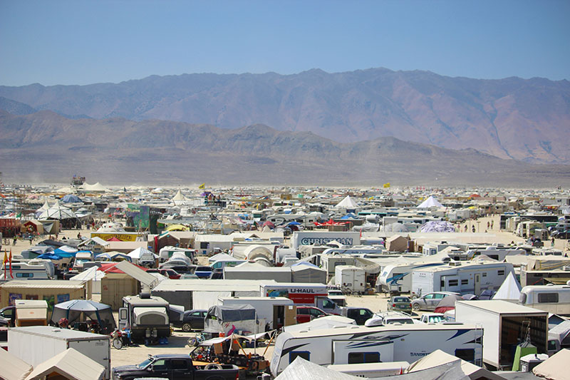 RVs fill the desert landscape as mountains rise in the horizon.