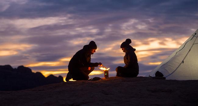 Couple using a BioLite CampStove 2 as the sun is setting behind them.
