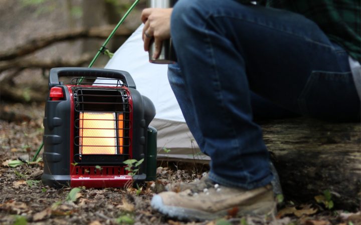 Man sitting on a log in the woods next to a tent and Mr Buddy Heater