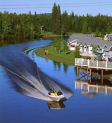 Daytime photograph of boat speeding down the Chena River with a house in background