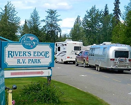 Sign of two RV's driving past the River's Edge RV Park sign with trees in background
