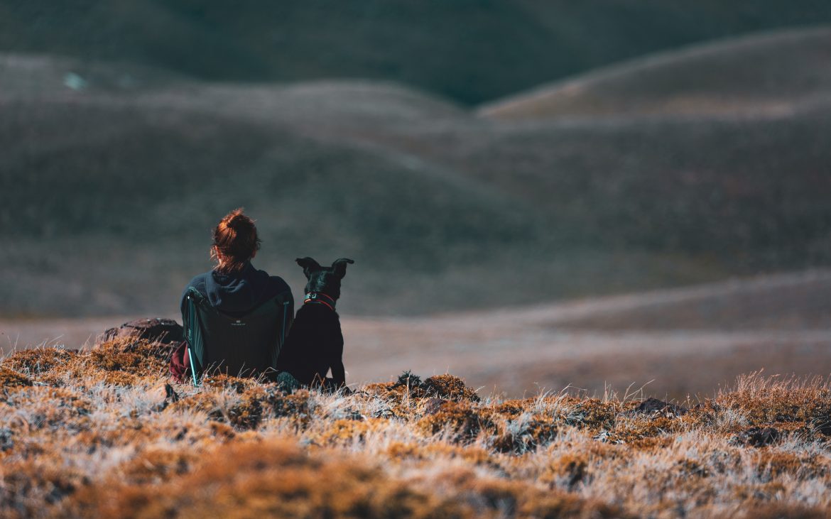 Woman sitting on mountain side with black dog
