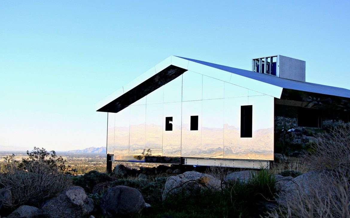 Mirrored covered house in the California desert reflecting land rocks and blue sky
