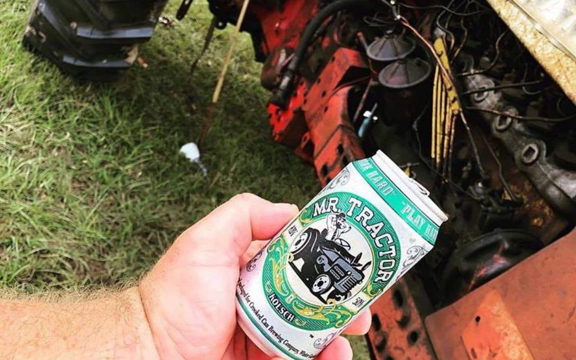 Man holding can beer near tractor