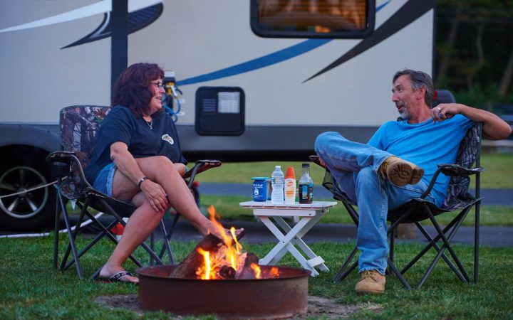 Young couple sitting beside campfire talking with RV in background