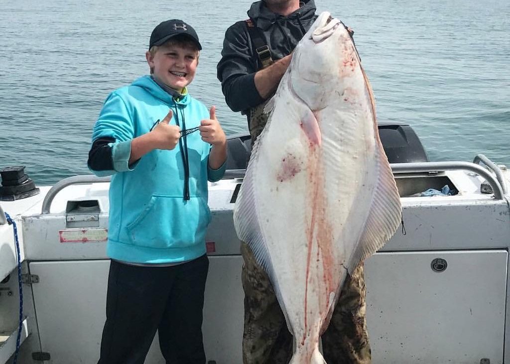Young boy standing beside his father holding a huge fish