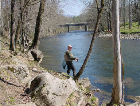 Man standing at edge of river bank fishing