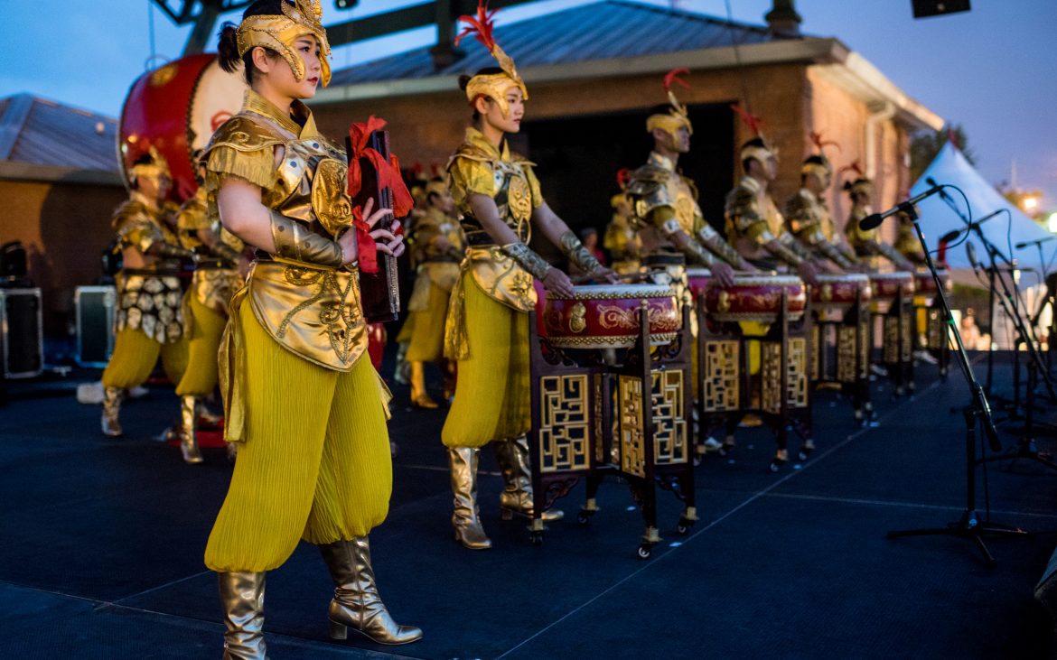 Performers on stage with hand drums dressed in yellow garb