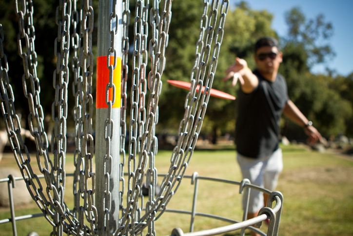 Disc golfer releases disc towards the basket for a successful putt.