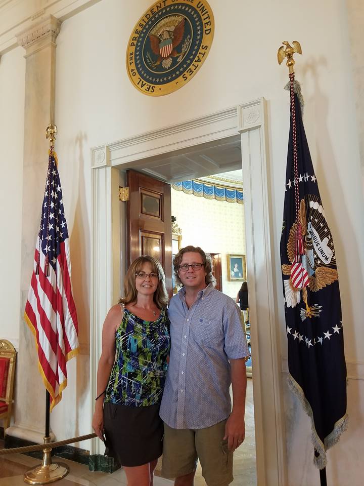 A couple stands beneath the presidential seal and are flanked by the U.S. flag and President of the United States Flag.