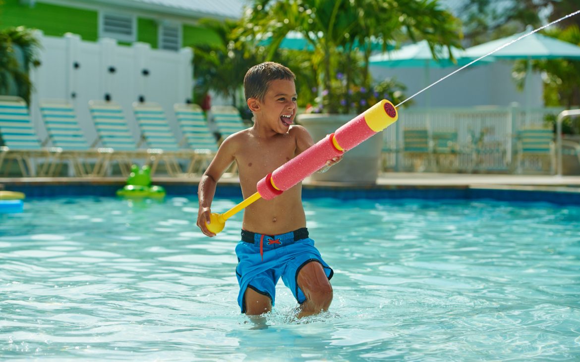 Young child in clear community pool shooting a water gun and laughing