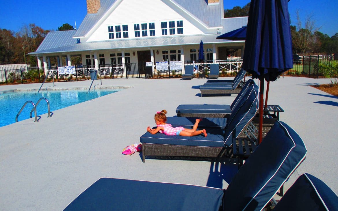 Small girl laying on blue lounger chair beside community pool