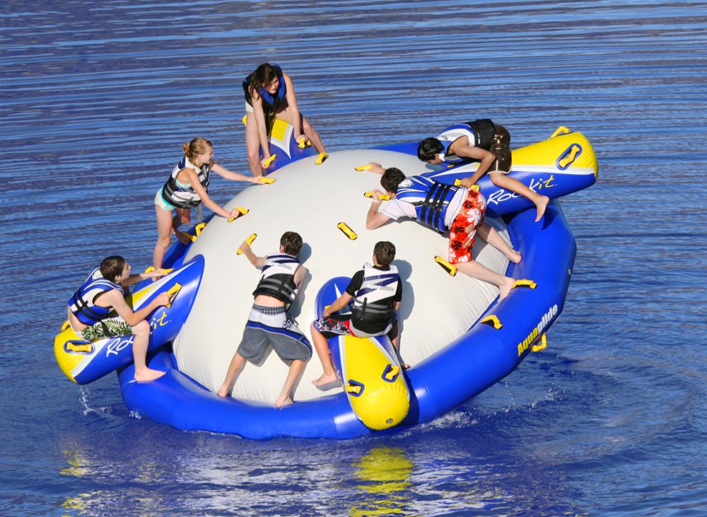 Group of kids playing on large inflatable water toy on lake