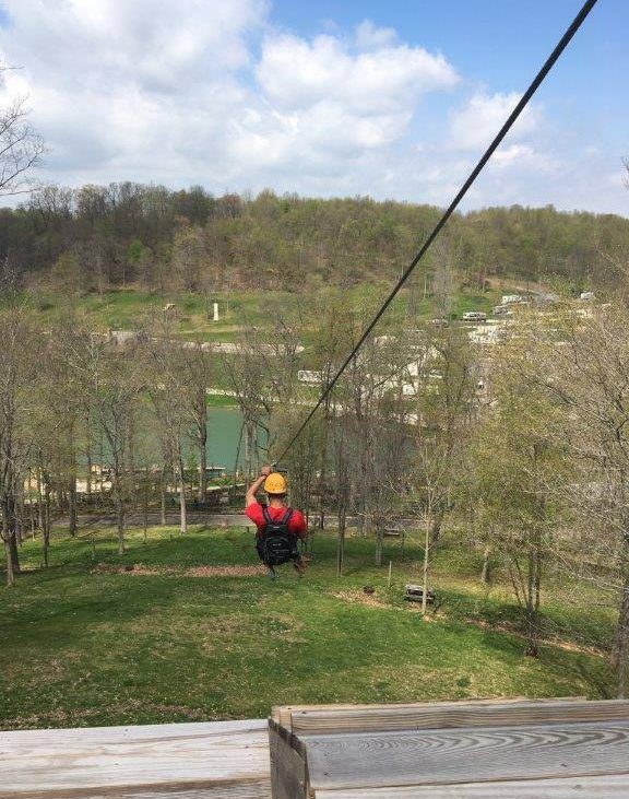 Camper in red jacket and yellow helmet cruising down zipline