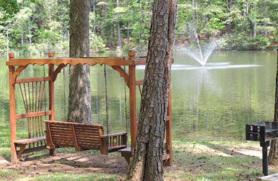 Wooden bench swing overlooking lake surrounded by lush green