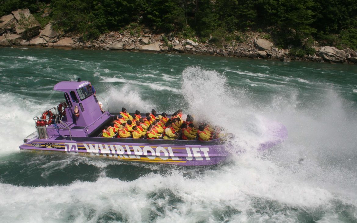 Large purple speedboat with many seats rushing through the water