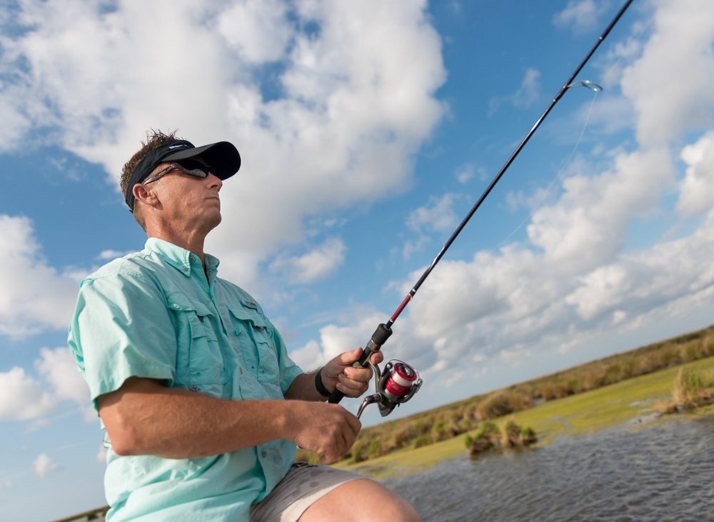Man in sunglasses and hat fishing under blue skies and clouds
