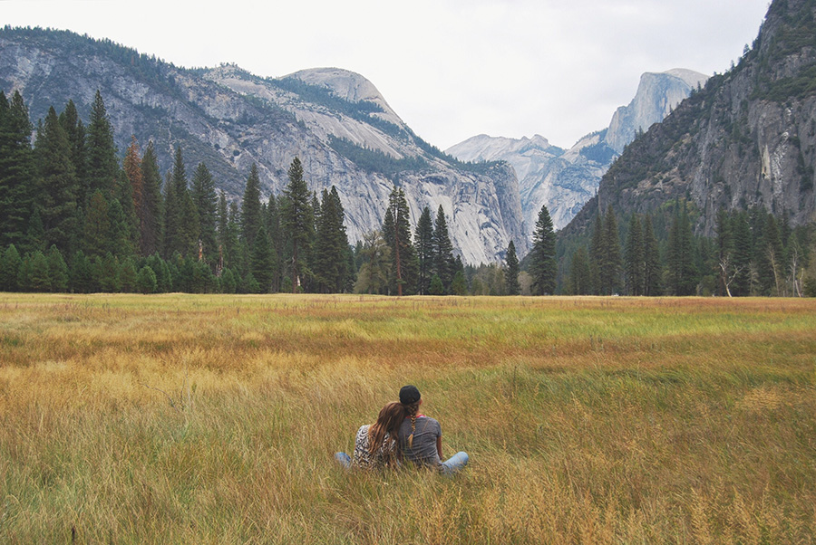A couple lounges on the grass with Half Dome in the distance.