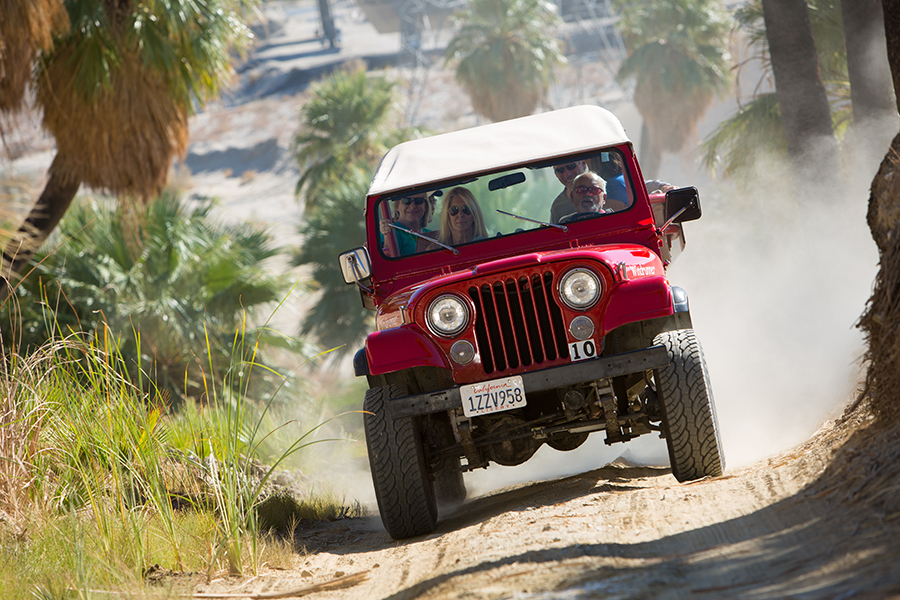 A red jeep churns up dust on a desert trail.