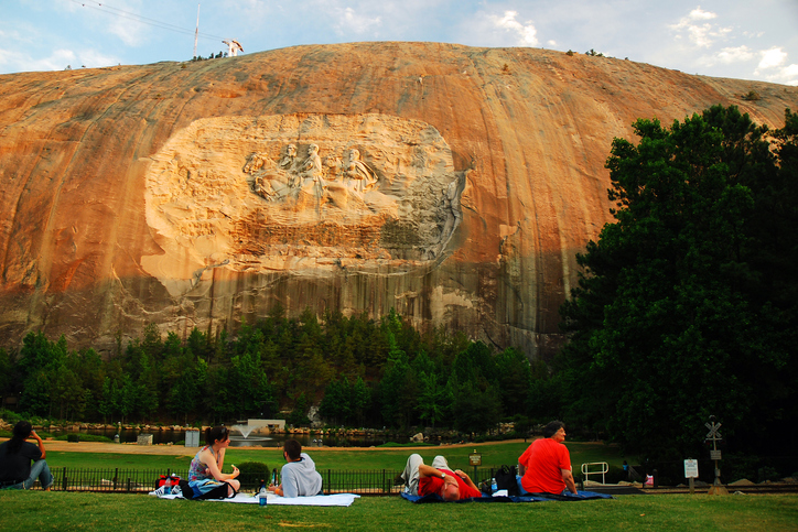 People have a picnic dinner under a large granite carving of Confederate Generals in Stone Mountain, Georgia