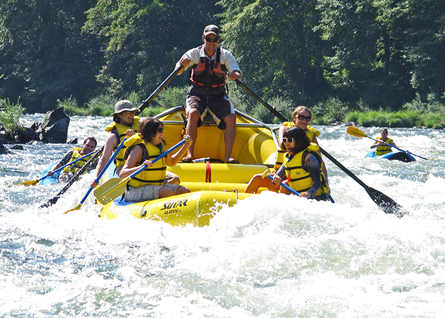 A yellow raft laden with fun seekers paddles on a rough part of the Rogue River.