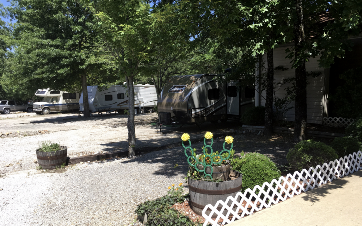 Several motorhomes parked in RV spots with lush green trees scattered