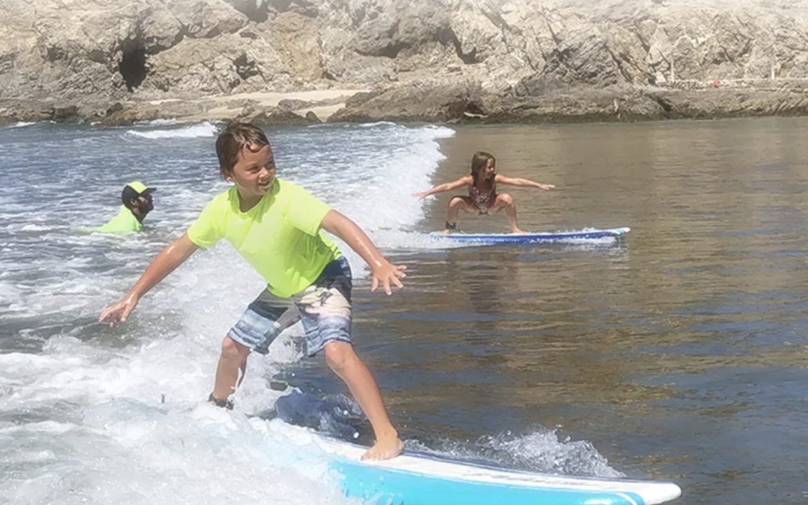 Young boy surfing with green shirt and young girl surfing next to him