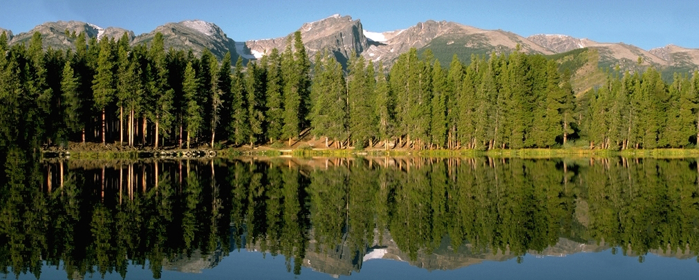 A mountain lake in the Colorado Rockies reflects the trees that line the shore. 