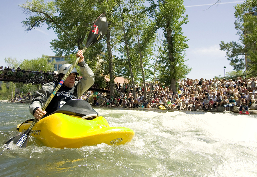 A kayaker propels his bright yellow kayak in front of a crowd through the whitewater in the Truckee Whitewater Park in Reno.