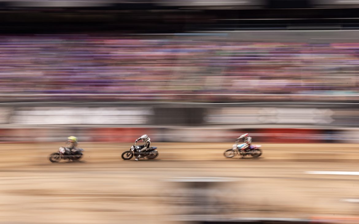 Three blurry motorcycle riders on dirt track racing