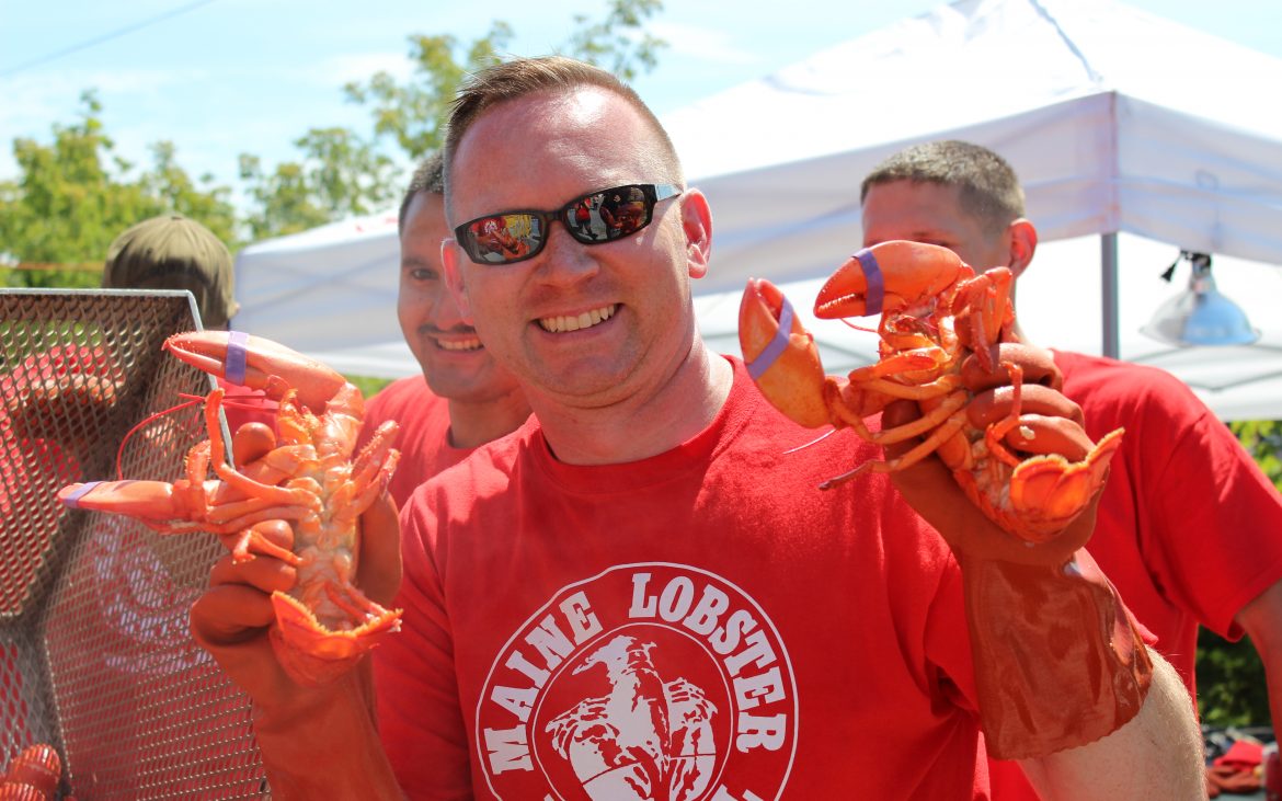 Man with red tshirt holding two lobsters smiling