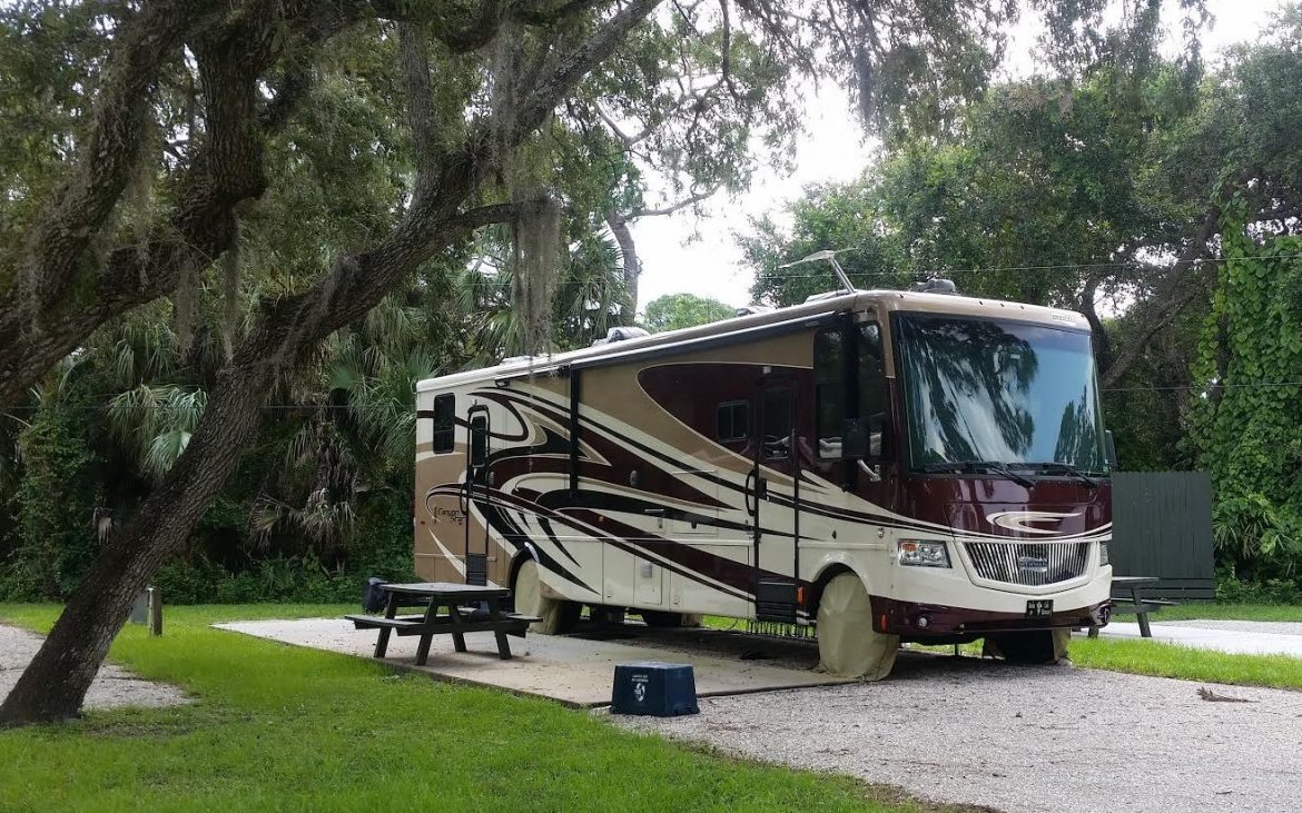 Large brown, tan and taupe RV alongside firepit and picnic table