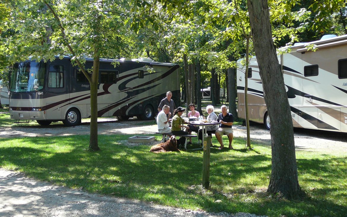 Group of adults enjoying a meal at picnic table alongside large RV