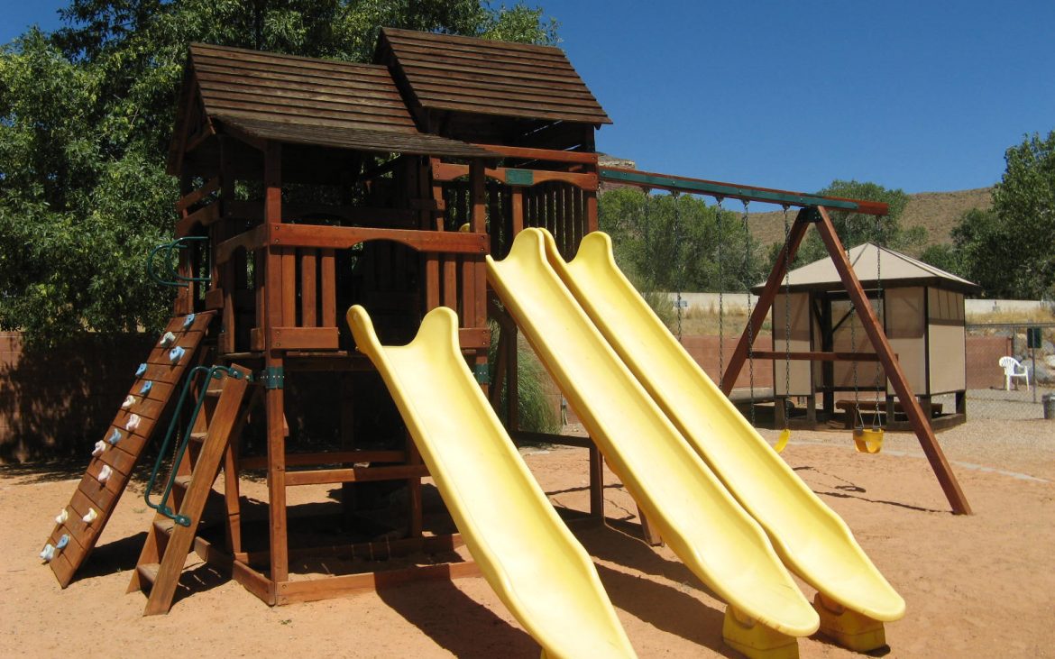 Wooden outside playhouse with three yellow slides on sandy area