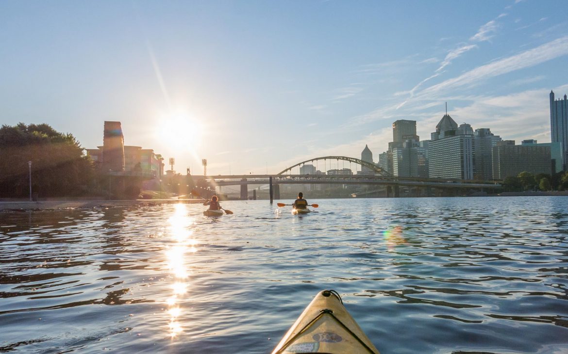 Sunrise over Pittsburgh river with kayakers heading toward bridge