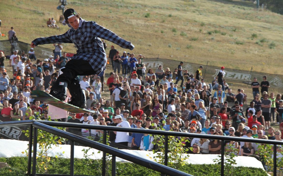 Young male snowboarder doing a trick on railing with crowd watching