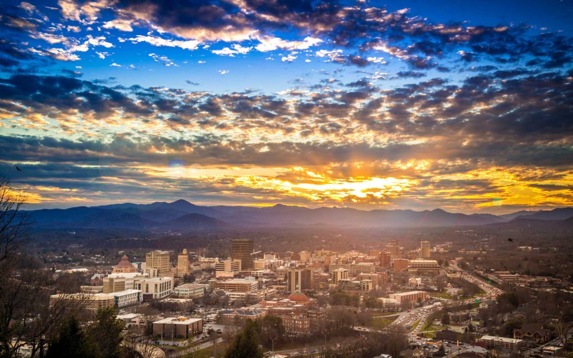 Epic Sunset over Downtown Asheville North Carolina NC cityscape with blue ridge mountain range and Mt. Pisgah featured in the background.